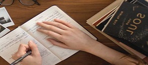 due mani scrivono un diario di fianco ad un'agenda di viaggi