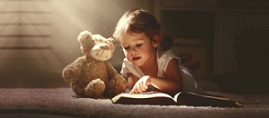 Bambino che legge un libro in compagnia di un orsacchiotto